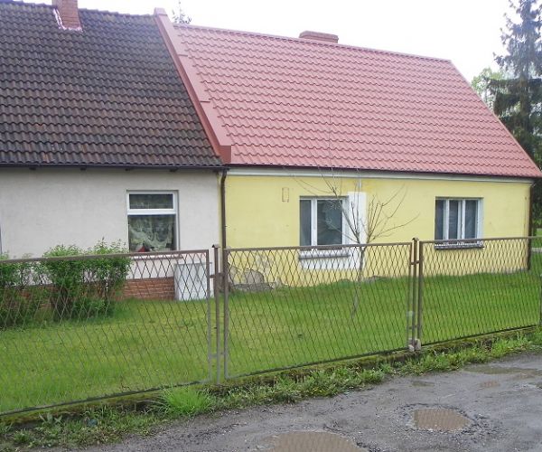Zdjęcie przedstawiające teren będący przedmiotem najmu, ogrodzony płotem teren i przylegający do niego budynek oraz zieleń.